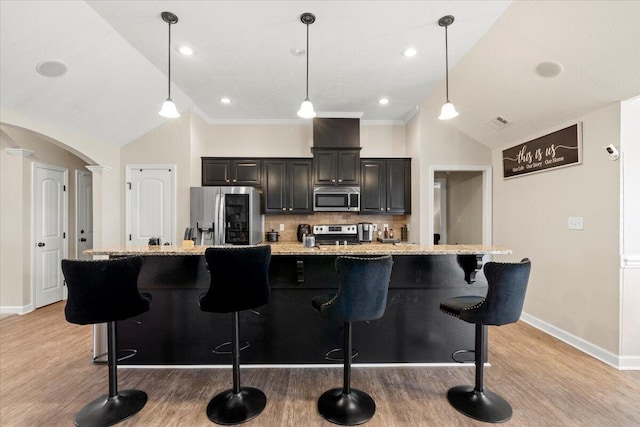 kitchen featuring a large island, a kitchen bar, decorative backsplash, appliances with stainless steel finishes, and ornamental molding