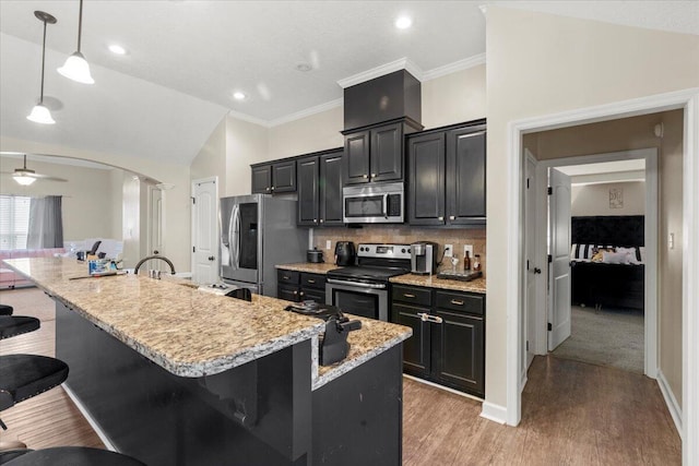 kitchen featuring a breakfast bar, pendant lighting, stainless steel appliances, and a center island with sink