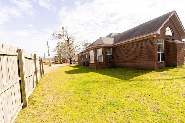 view of home's exterior with brick siding, fence, a lawn, and central air condition unit