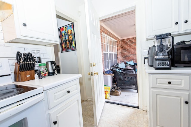 kitchen with light countertops, white range with electric cooktop, brick wall, and white cabinetry