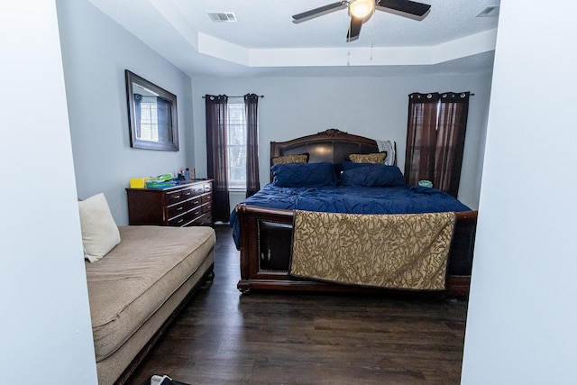 bedroom with a tray ceiling, wood finished floors, visible vents, and a ceiling fan