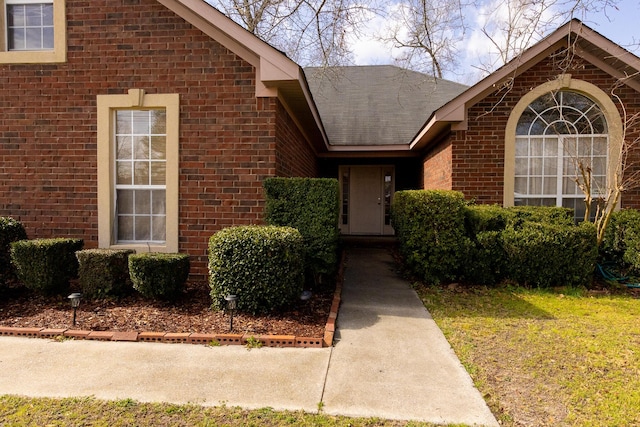 entrance to property featuring roof with shingles and brick siding