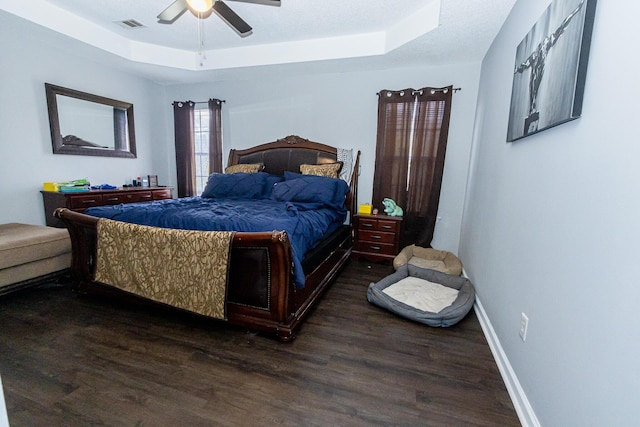 bedroom featuring baseboards, visible vents, a ceiling fan, a raised ceiling, and dark wood finished floors