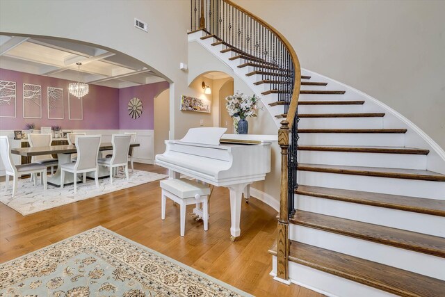 stairway featuring visible vents, coffered ceiling, arched walkways, an inviting chandelier, and wood finished floors
