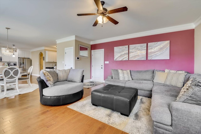 living room with baseboards, light wood-type flooring, ceiling fan with notable chandelier, and crown molding