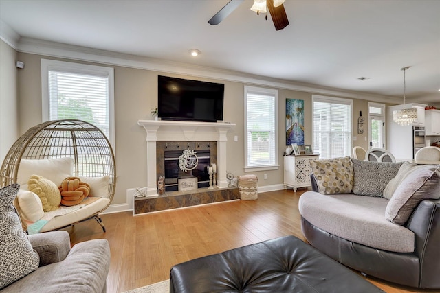 living area with crown molding, ceiling fan with notable chandelier, baseboards, and a fireplace