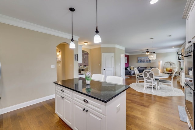 kitchen featuring crown molding, a center island, arched walkways, hardwood / wood-style floors, and open floor plan