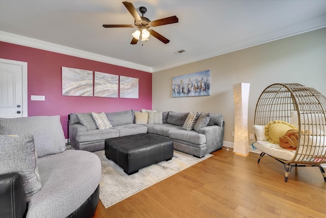 living room featuring visible vents, light wood-style floors, ceiling fan, baseboards, and ornamental molding