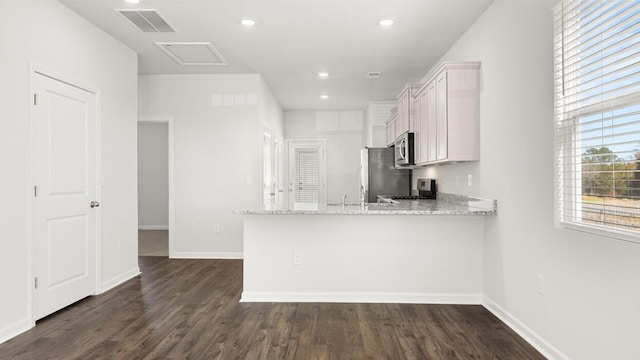 kitchen with appliances with stainless steel finishes, dark wood-type flooring, light stone counters, white cabinetry, and kitchen peninsula