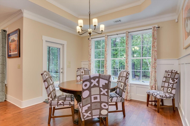 dining area featuring wood-type flooring, crown molding, a tray ceiling, and an inviting chandelier