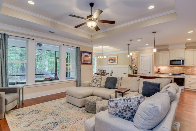 living room with ceiling fan with notable chandelier, a raised ceiling, ornamental molding, and wood-type flooring