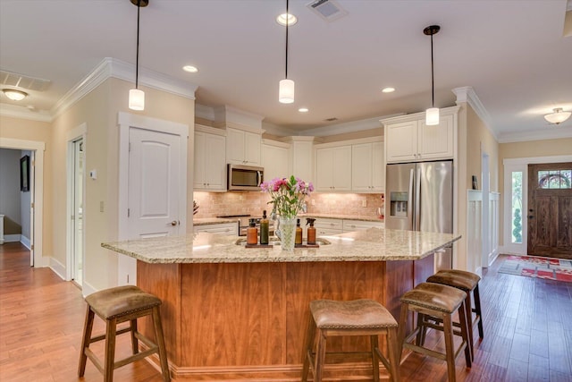 kitchen with hanging light fixtures, tasteful backsplash, light stone counters, a large island with sink, and appliances with stainless steel finishes