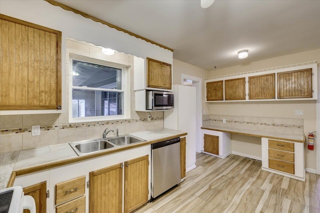 kitchen featuring sink, appliances with stainless steel finishes, built in desk, light hardwood / wood-style floors, and decorative backsplash