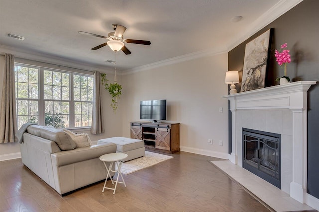 living room with ornamental molding, wood-type flooring, ceiling fan, and a fireplace