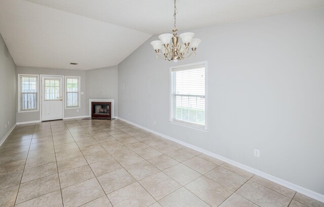 unfurnished living room with a wealth of natural light, light tile patterned floors, vaulted ceiling, and a notable chandelier