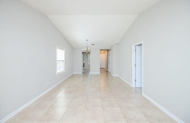 empty room featuring lofted ceiling, light tile patterned floors, and a chandelier