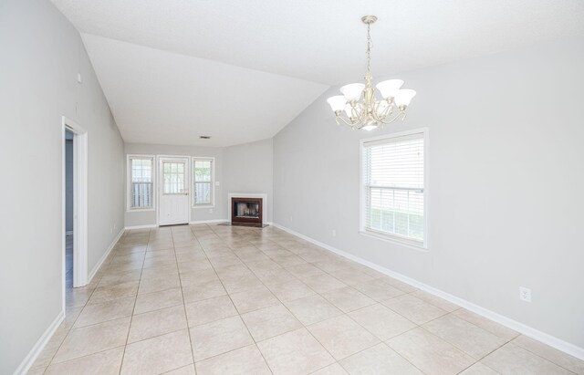 unfurnished living room with plenty of natural light, light tile patterned flooring, lofted ceiling, and an inviting chandelier