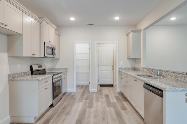 kitchen with white cabinets, sink, light hardwood / wood-style flooring, light stone countertops, and appliances with stainless steel finishes