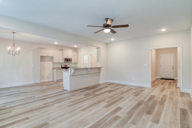 unfurnished living room with ceiling fan with notable chandelier and light hardwood / wood-style floors