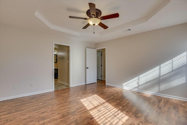 spare room featuring a raised ceiling, hardwood / wood-style flooring, and ceiling fan