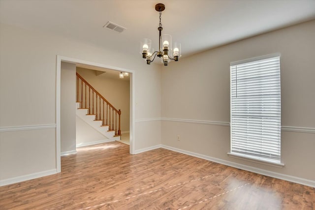 spare room featuring wood-type flooring and a notable chandelier