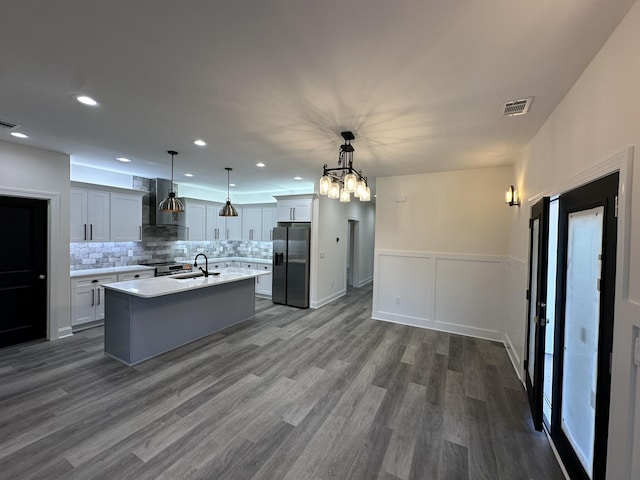 kitchen featuring stainless steel fridge, sink, wall chimney range hood, pendant lighting, and an island with sink