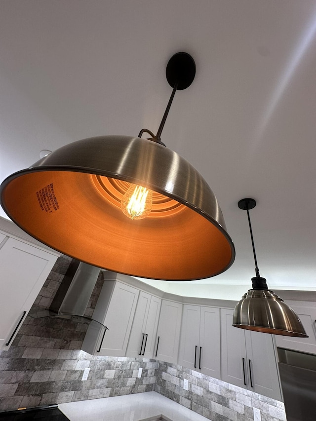 details featuring decorative backsplash, white cabinets, and pendant lighting