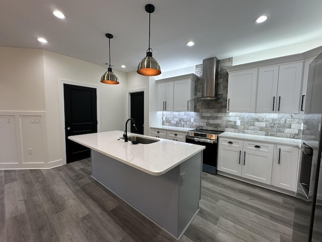 kitchen featuring pendant lighting, a kitchen island with sink, wall chimney range hood, sink, and electric stove