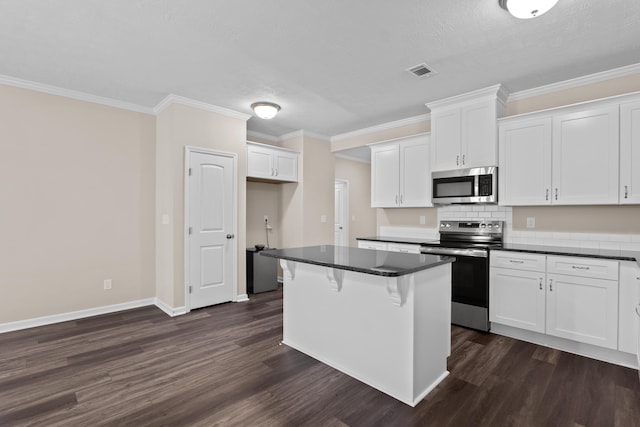 1006 Rosendale Dr, Hephzibah, GA 30815 - kitchen featuring stainless steel appliances, dark countertops, dark wood-style floors, white cabinets, and ornamental molding
