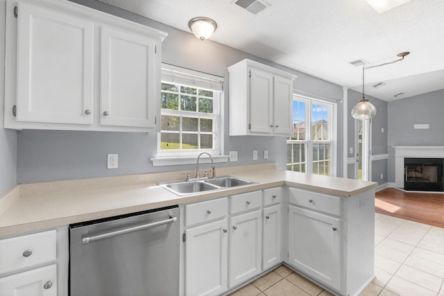 kitchen featuring visible vents, dishwasher, a sink, light countertops, and a peninsula