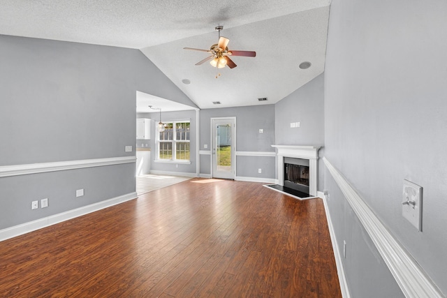 unfurnished living room with wood finished floors, baseboards, a fireplace with raised hearth, a ceiling fan, and vaulted ceiling