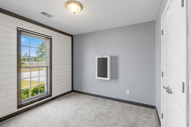 carpeted spare room featuring wooden walls, a textured ceiling, visible vents, and baseboards