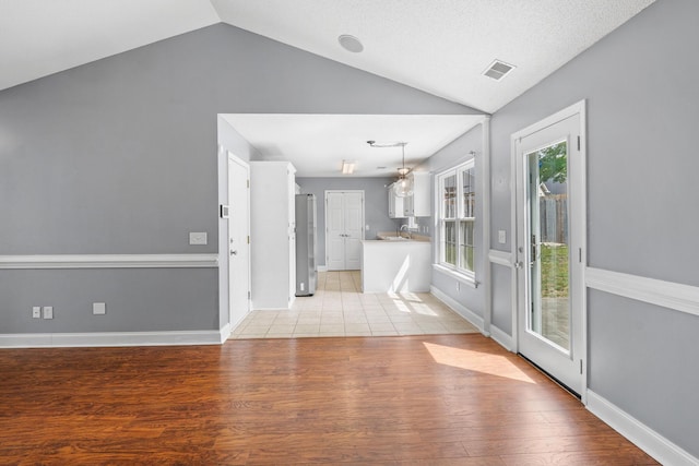 unfurnished living room with baseboards, vaulted ceiling, light wood-style flooring, and visible vents