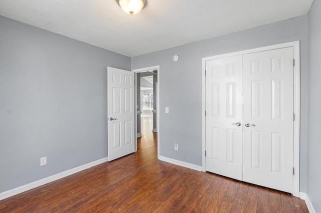 unfurnished bedroom with baseboards, dark wood finished floors, and a closet