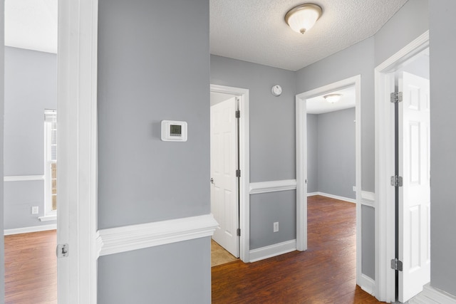 hallway with a textured ceiling, baseboards, and wood finished floors