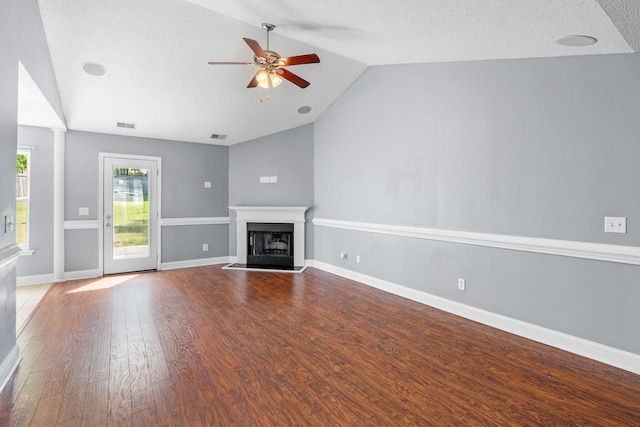 unfurnished living room with visible vents, wood finished floors, ceiling fan, a fireplace with raised hearth, and vaulted ceiling