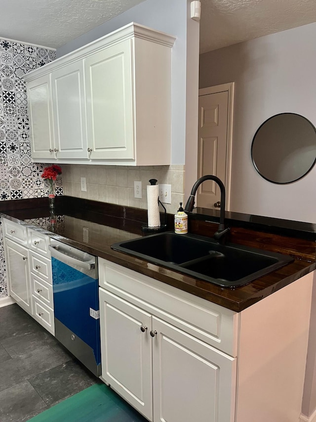 kitchen with dishwasher, dark countertops, a sink, and white cabinetry