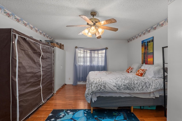 bedroom with ceiling fan, wood finished floors, and a textured ceiling