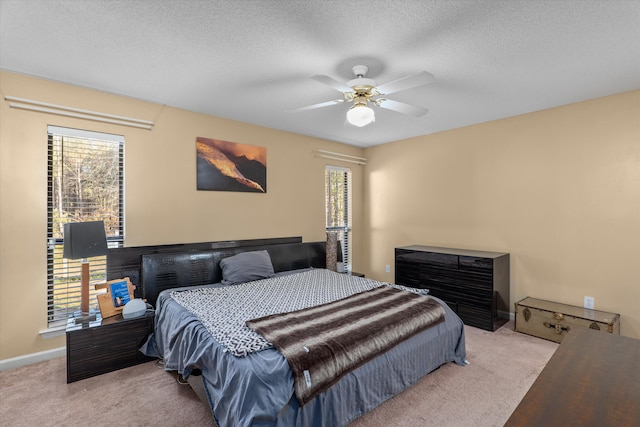 carpeted bedroom with ceiling fan, multiple windows, baseboards, and a textured ceiling