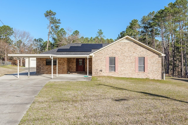 ranch-style home featuring an attached carport, a front lawn, brick siding, and roof mounted solar panels