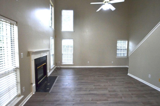 unfurnished living room with ceiling fan, wood finished floors, a high end fireplace, a high ceiling, and baseboards
