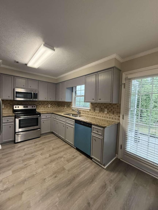 kitchen with appliances with stainless steel finishes, gray cabinetry, a sink, crown molding, and backsplash