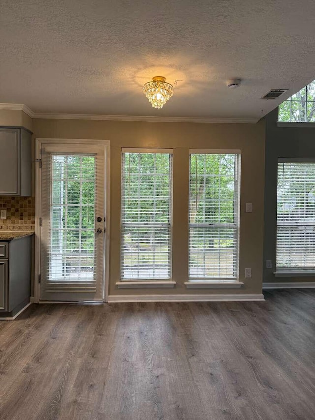 entryway with a textured ceiling, wood finished floors, healthy amount of natural light, baseboards, and crown molding