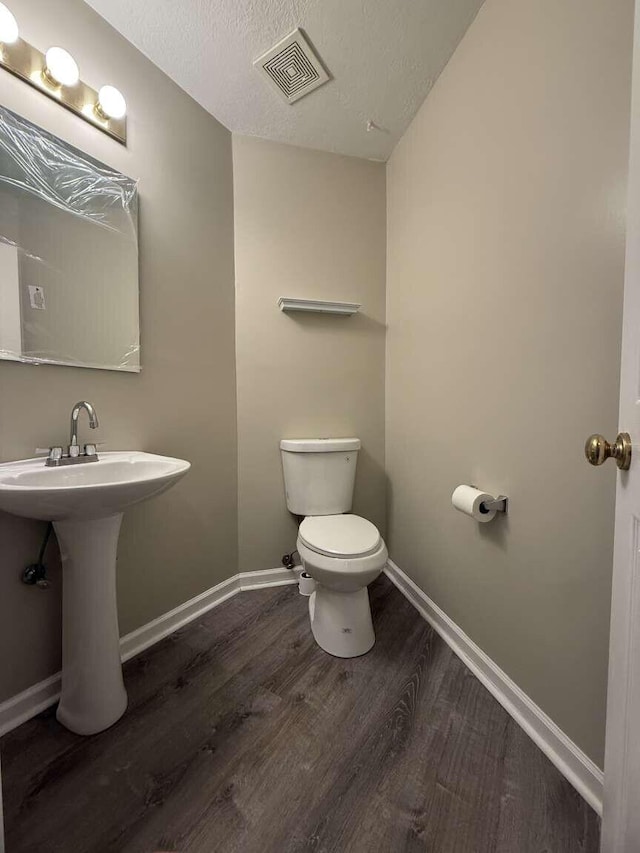 half bathroom with toilet, wood finished floors, baseboards, a textured ceiling, and a sink