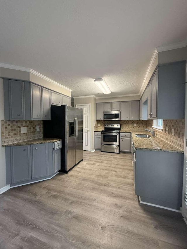 kitchen with appliances with stainless steel finishes, gray cabinets, a sink, ornamental molding, and light wood finished floors