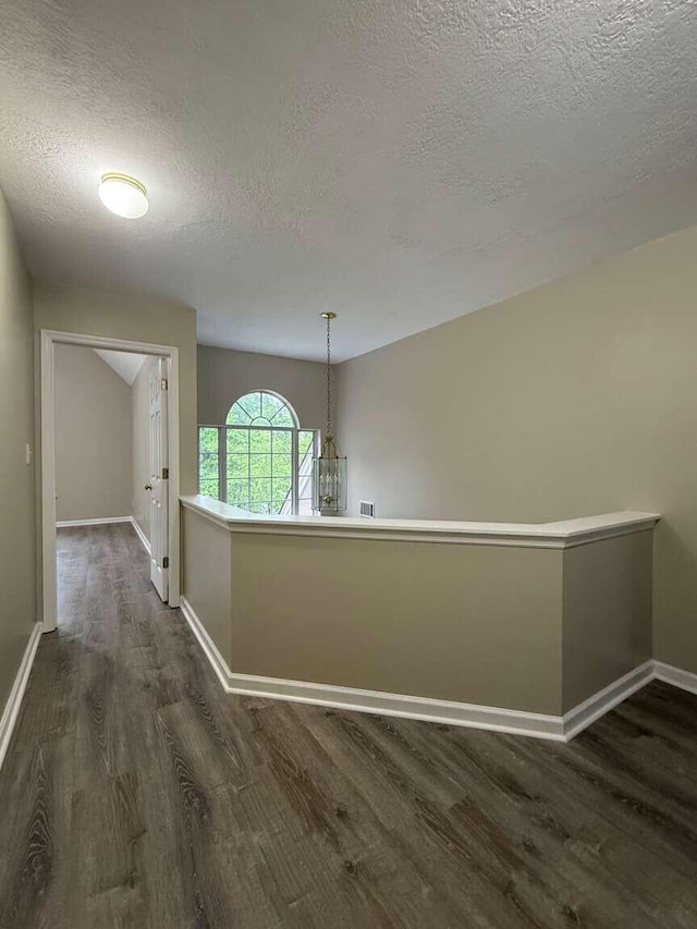 hall featuring a textured ceiling, dark wood-style floors, and baseboards