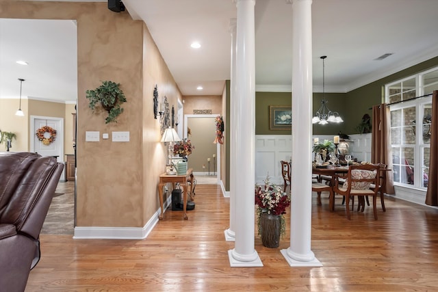 hallway with light hardwood / wood-style floors, ornate columns, a notable chandelier, and crown molding