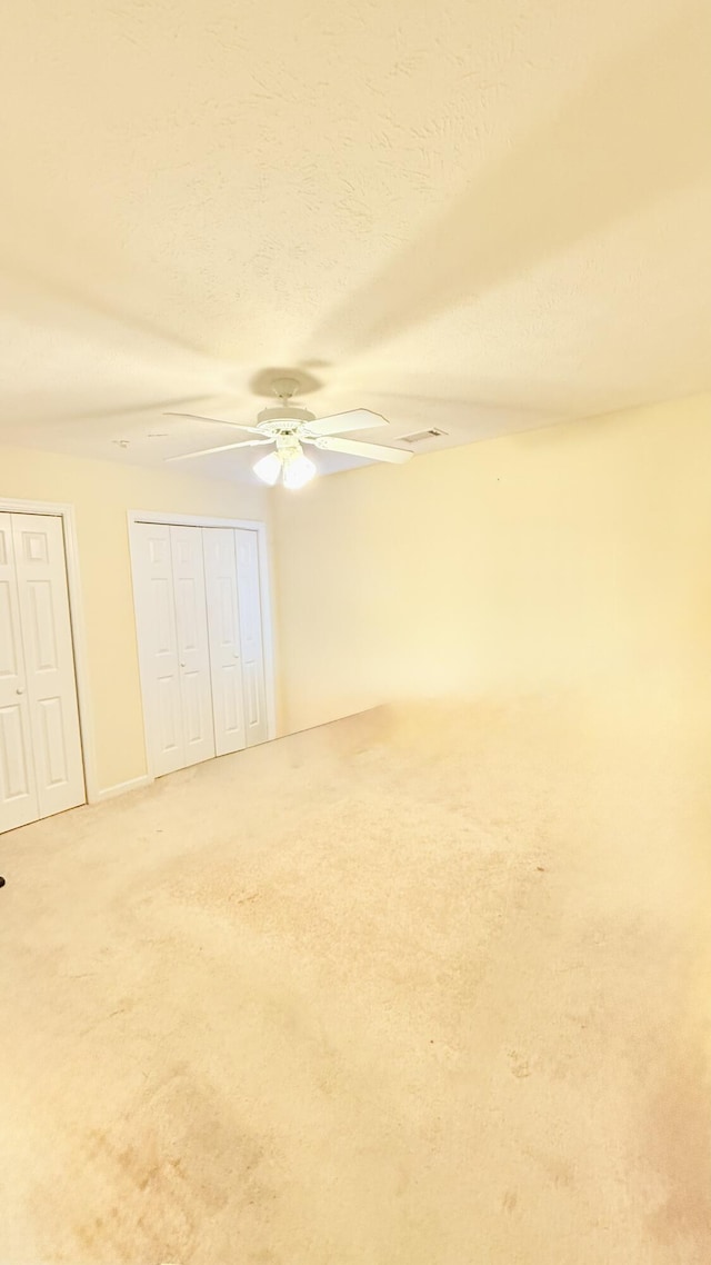 unfurnished bedroom featuring multiple closets, carpet flooring, a textured ceiling, and a ceiling fan