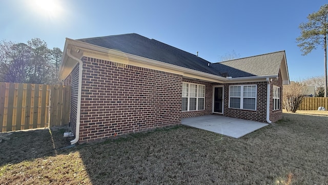 back of house with brick siding, a yard, a shingled roof, a patio area, and fence