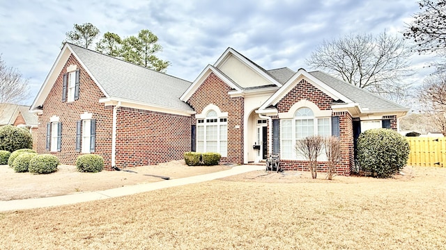 view of front of property with brick siding, a shingled roof, and fence